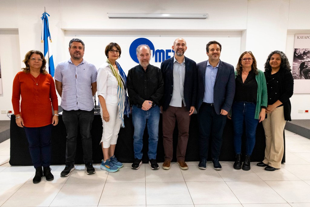 Grupo de personas de pie en un evento en la Universidad Metropolitana para la Educación y el Trabajo (UMET), con una bandera argentina y un fondo que muestra el logo de UMET.