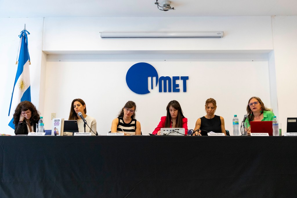 Panel de discusión en la Universidad Metropolitana para la Educación y el Trabajo (UMET) con cinco presentadoras, micrófonos y material de apoyo en la mesa, en un ambiente académico.