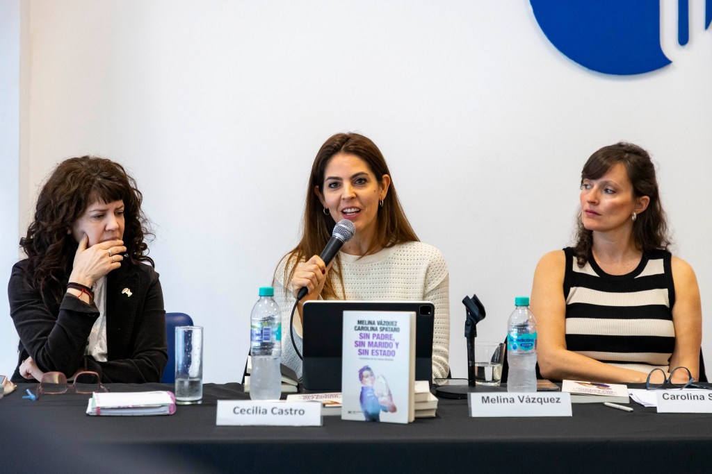 Tres ponentes en una mesa de debate, con micrófono y libros sobre la mesa, durante un evento en la Universidad Metropolitana para la Educación y el Trabajo.