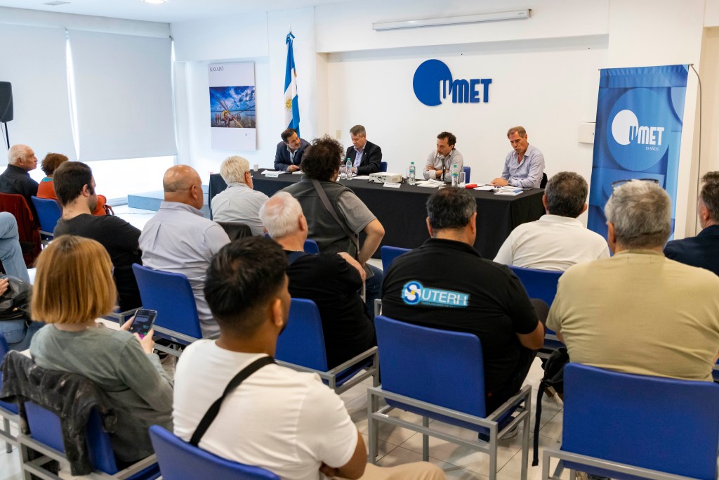 Un panel de debate en la Universidad Metropolitana para la Educación y el Trabajo (UMET) con participantes en una sala llena, discutiendo temas de investigación y desarrollo.