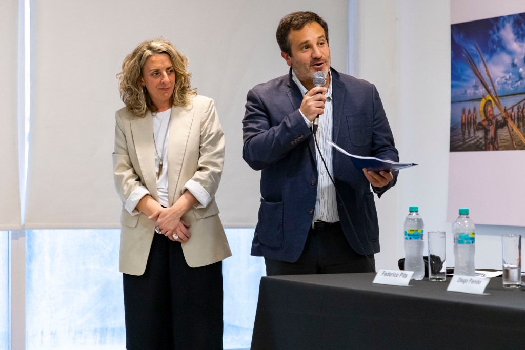 Dos presentadores en una mesa de debate, uno de ellos hablando por un micrófono mientras la otra persona escucha atentamente.